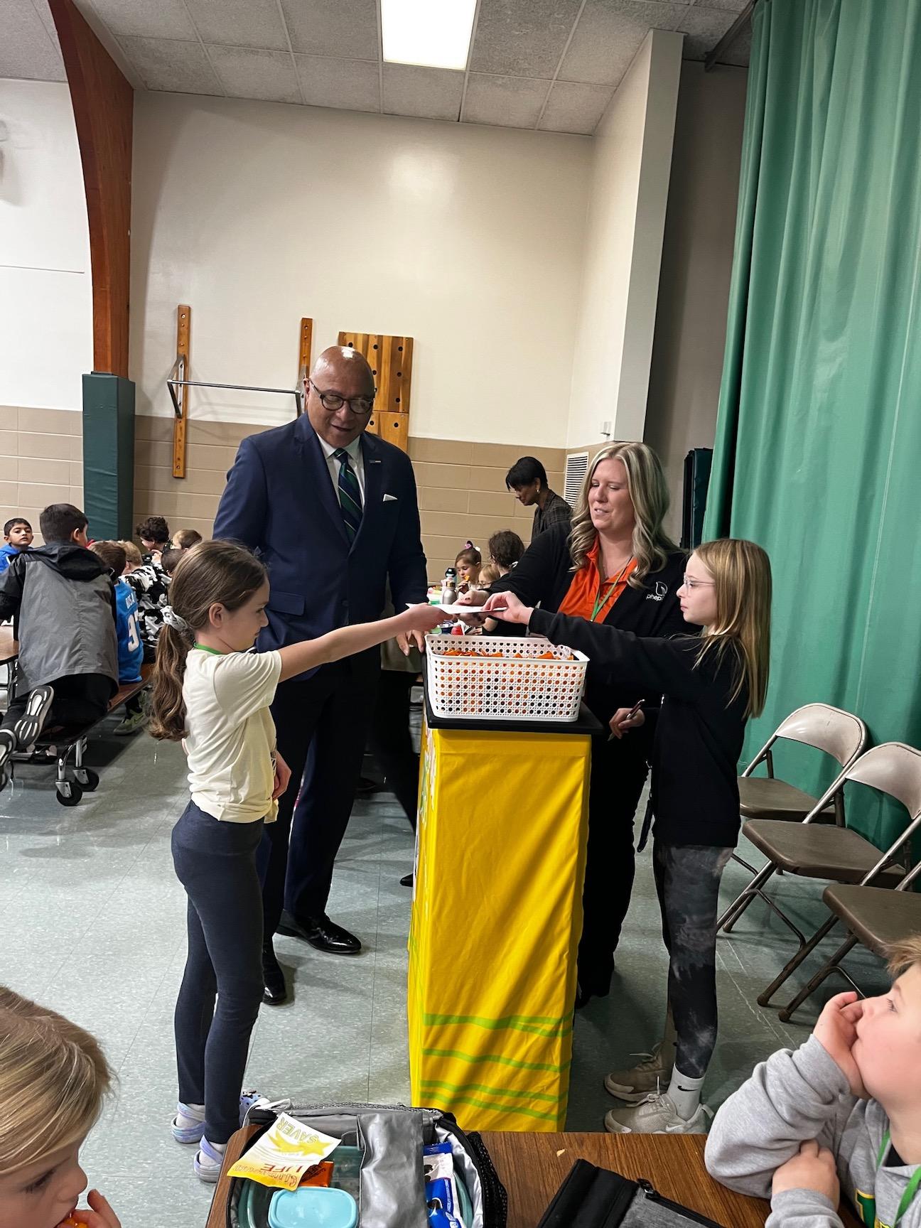Mr. DeFoor and Ms. Harr observe while third-grader Norah Barton (left) presents her deposit to the ‘student teller’ Jenna Donis (right)