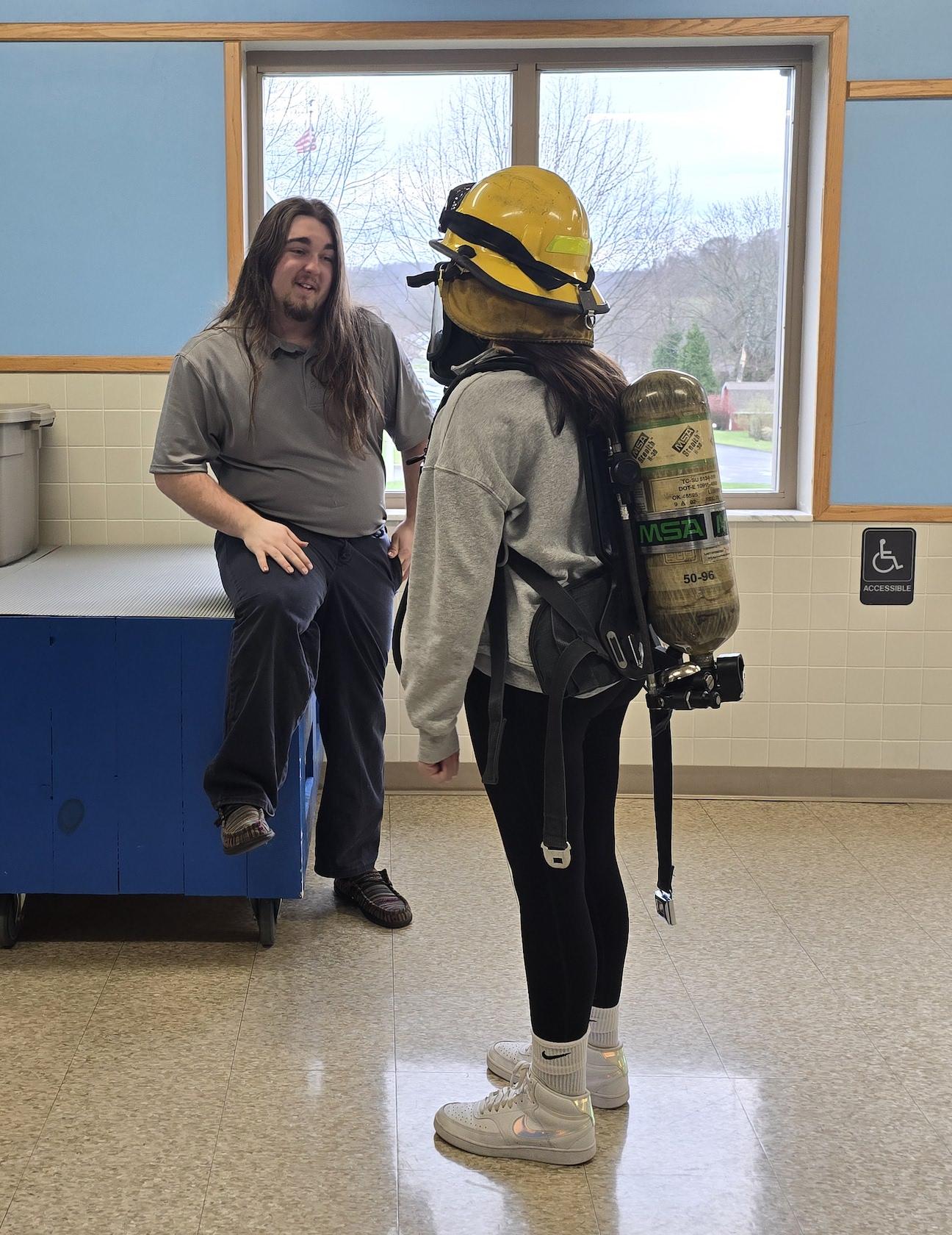Penn-Trafford/CWCTC Protective Services student Hayden Inman        helps Harrison Park student, Delaney Flebotte, gear up in the fire fighting equipment